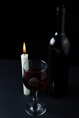 Wine and candle on a dark background. Creative photo of red wine on a black background. Wine by candlelight