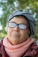 a slightly recent face of an elderly woman in a gray beret and a pink scarf on a sunny day