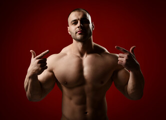 Strong muscular unshaved brutal man, bodybuilder standing with naked chest and pointing fingers at...