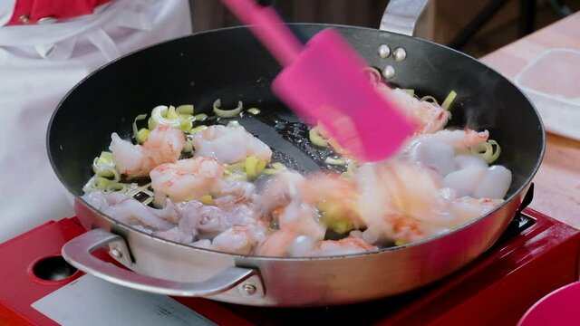 Close up view, chef holding kitchen spatula stirring frying on electric stove seafood, prawns, squids and leek. Food preparation process concept