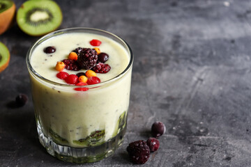 Yogurt with berry and kiwi in a glass. Fruit and berry smoothie. Milkshake with kiwi, raspberry, blueberry and banana Healthy food. Dark background. Copy space.