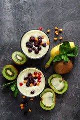 Yogurt with berry and kiwi in a glass. Fruit and berry smoothie. Milkshake with kiwi, raspberry, blueberry and banana. Top view Healthy food. Dark background. Copy space.