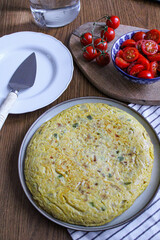 Spanish Omelette dinner from top view. Sliced tortilla on table with a served slice. Side salad made of tomatoes. 