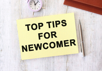 TOP TIOS FOR NEWCOMER text written in a notebook lying on a wooden work table.
