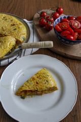 Spanish Omelette dinner from top view. Sliced tortilla on table with a served slice. Side salad made of tomatoes. 