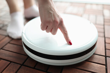 Woman turning on finger of robot vacuum cleaner closeup