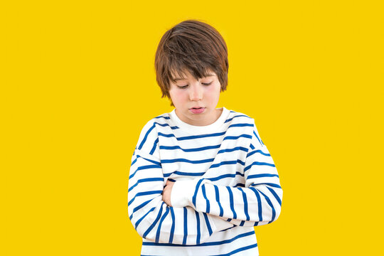 Sad, upset, frustrated child  in casual striped t shirt posing isolated on yellow orange background, looking down, studio portrait. People emotions lifestyle concept. Mock up copy space.