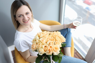 Woman with bouquet of roses sitting with glass of wine in hand