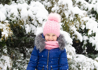 A girl in a pink hat plays with snow. Holidays with a child in winter