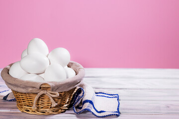 White Chicken eggs in a Straw basket on a pink background with piece of cloth, Natural Product