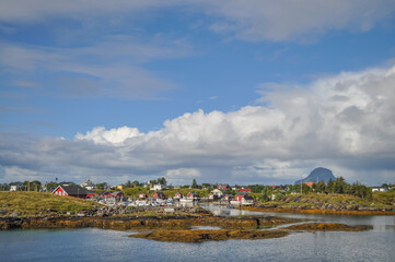 Obraz premium View from ferry to the small fishermen village on island in Helgeland archipelago in the Norwegian sea on sunny summer morning. Silhouette of Lovund island on the background 