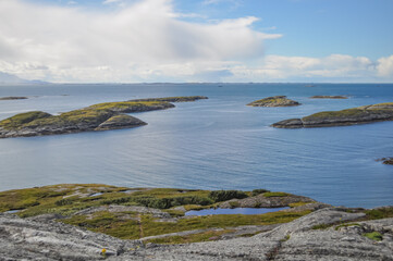 Fototapeta na wymiar View from Lovund hills to the rocky coastline and the small green rocky islands of Lovund archipelago in the Norwegian sea on sunny summer morning. White clouds over the blue sea. 