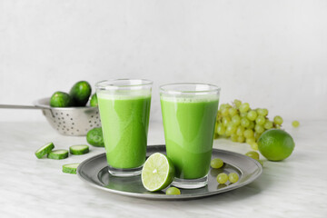 Glasses of tasty green smoothie and ingredients on light background