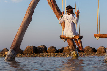 Back view female sitting on the swing on sea shore. Concept of waiting or loneliness