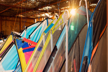 Windsurfing sails storage on a beach watersports facility. Surfer boards on shelf lie  under the roof for rental. Colorful sails background in sunlight