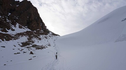 A large group of climbers climb to the top. A camp of tents is set up. Snowy mountains in summer. View of the trail with a group of tourists. Queue for the peak. Shooting from above from a drone.