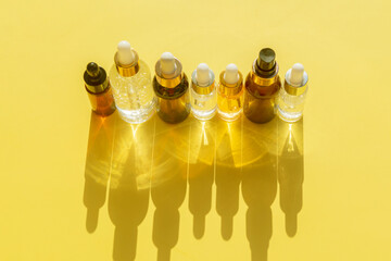 set of different bottles with beauty serum, hyaluronic acid and vitamins on a yellow background