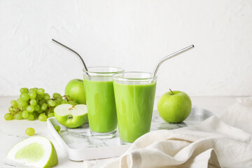 Glasses of healthy green smoothie and ingredients on light background