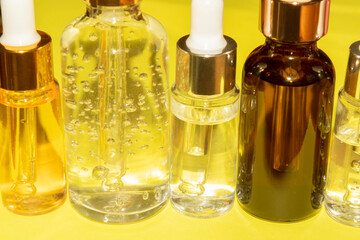 set of different bottles with beauty serum, hyaluronic acid and vitamins on a yellow background