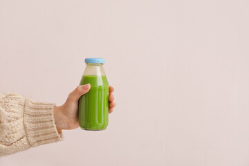 Woman holding bottle of healthy green smoothie on light background