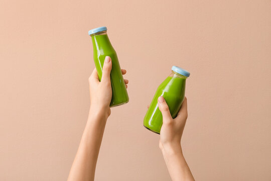 Woman holding bottles of healthy green smoothie on color background