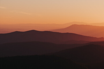Fototapeta premium A vibrant citrus orange, yellow, deep purple sunset over the layers of the Appalachian Mountain range from Shenandoah National Park, Virginia, USA.