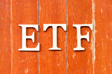 Alphabet letter in word ETF (abbreviation of Exchange Traded Fund) on old red color wood plate background