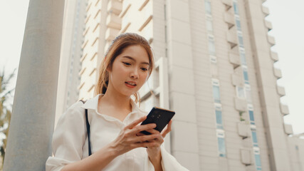 Successful young Asia businesswoman in fashion office clothes using smart phone and typing text message while walking alone outdoors in urban modern city in the morning. Business on the go concept.