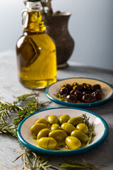 Natural black and green olives with rosemary, basil and olive tree leaves on blue wooden background.