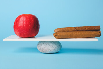 Apple and cigars on teeterboard against color background. Concept of balance