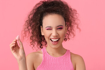 Beautiful young African-American woman with makeup sponge on color background