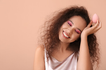 Fototapeta premium Beautiful young African-American woman with makeup sponge on color background
