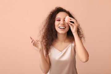 Beautiful young African-American woman with makeup sponge on color background