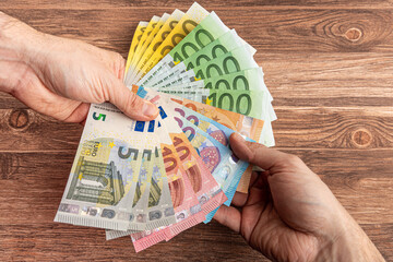 Viele Eurobanknoten werden vor Holzhintergrund von einer Hand in die andere Hand übergeben