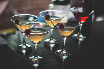 View of different coloured alcohol beverage cocktail drinks setting on bar counter in the night club party, tequila, glasses with martini, vodka, spritz and others on decorated catering banquet table
