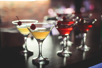 View of different coloured alcohol beverage cocktail drinks setting on bar counter in the night club party, tequila, glasses with martini, vodka, spritz and others on decorated catering banquet table