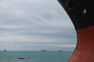 Seascape with rusty bow of large ship with draft scale numbering, large dry-cargo ships in the...