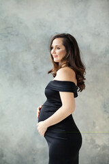 Fototapeta premium Nice pregnant woman in black dress on gray background portrait