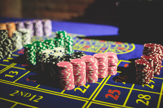 A close-up vibrant image of multicolored casino table with roulette in motion, with casino chips. the hand of croupier, money and a group of gambling rich wealthy people playing in the background