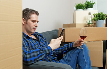 Man with smartphone and glass of wine in new apartment.