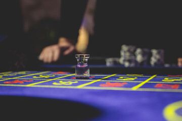 Naklejka premium A close-up vibrant image of multicolored casino table with roulette in motion, with casino chips. the hand of croupier, money and a group of gambling rich wealthy people playing in the background