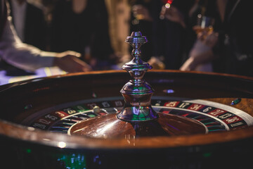 Obraz premium A close-up vibrant image of multicolored casino table with roulette in motion, with casino chips. the hand of croupier, money and a group of gambling rich wealthy people playing in the background
