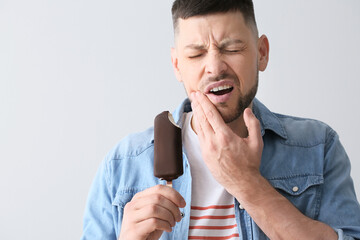 Man with sensitive teeth and ice-cream on grey background