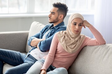 Sad young woman in hijab sitting by her sad husband