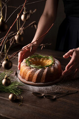 A Christmas cake on a wooden table. Country style. Hugge. Hands in the frame. Dark photo