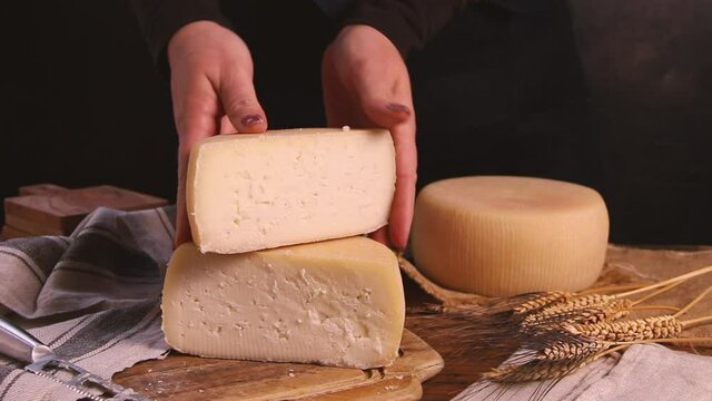 Women hands showing fresh homemade cheese on a wooden board with a cheese knife close up