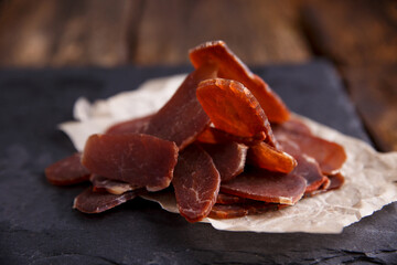 Jerky with spices on a black stone cutting board, dark background. Beer snack.