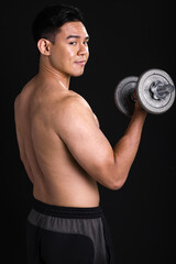 Fototapeta na wymiar Portrait of asian muscular man standing and lifting dumbbell on black background
