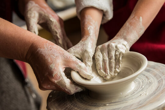Senior potter teaching a little girl the art of pottery. Child working with clay Creating ceramic pot on sculpting wheel