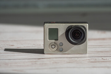 An old shabby and dusty little action camera stands against a wooden background with a long shadow....